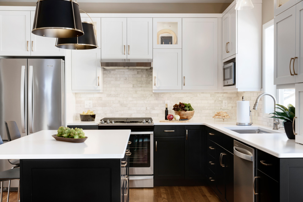 Mid-sized transitional l-shaped medium tone wood floor and brown floor eat-in kitchen photo in Minneapolis with an undermount sink, recessed-panel cabinets, black cabinets, quartz countertops, beige backsplash, stone tile backsplash, stainless steel appliances, an island and white countertops
