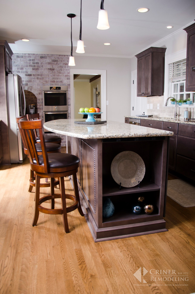 Transitional light wood floor eat-in kitchen photo with shaker cabinets, dark wood cabinets, granite countertops, beige backsplash, glass tile backsplash, stainless steel appliances and an island