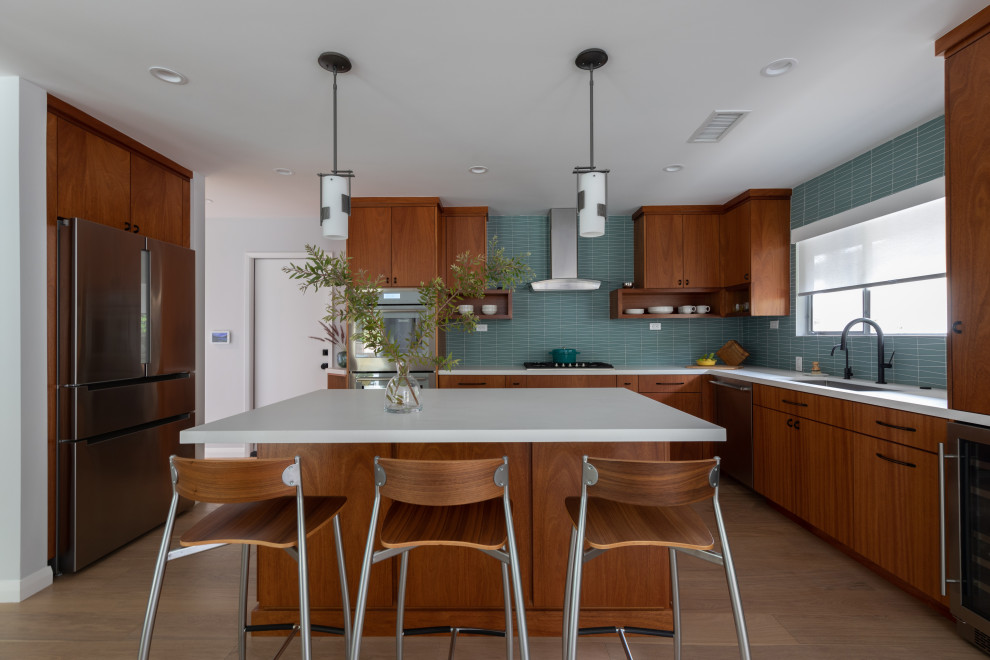 Design ideas for a mid-sized midcentury open plan kitchen in Los Angeles with an undermount sink, flat-panel cabinets, medium wood cabinets, quartz benchtops, blue splashback, glass tile splashback, stainless steel appliances, light hardwood floors, with island and white benchtop.