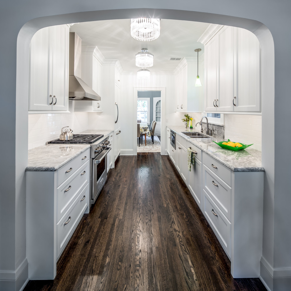 This is an example of a mid-sized traditional galley separate kitchen in Minneapolis with an undermount sink, shaker cabinets, white splashback, white cabinets, granite benchtops, subway tile splashback, dark hardwood floors, no island and brown floor.