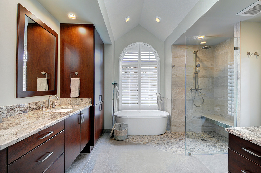 Large beach style master bathroom in Tampa with an undermount sink, flat-panel cabinets, dark wood cabinets, granite benchtops, a freestanding tub, a curbless shower, a two-piece toilet, gray tile, porcelain tile, white walls and pebble tile floors.