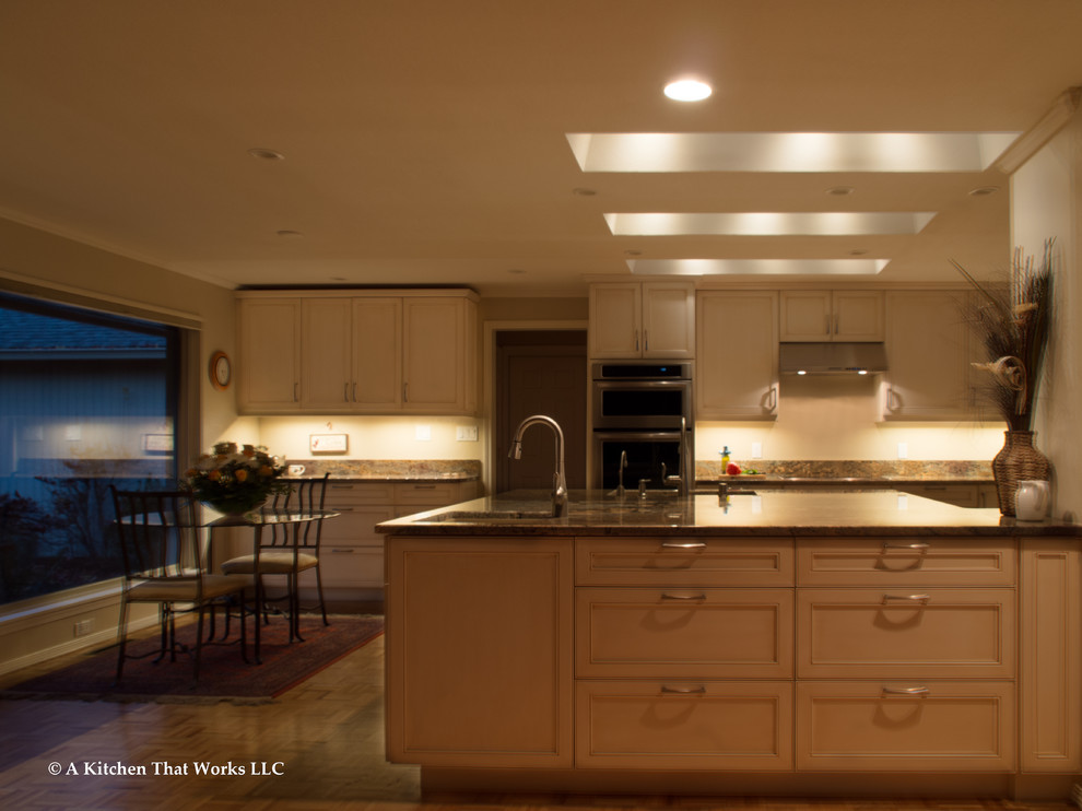 Large transitional u-shaped medium tone wood floor and brown floor eat-in kitchen photo in Seattle with an undermount sink, recessed-panel cabinets, white cabinets, granite countertops, stone slab backsplash, stainless steel appliances, an island, brown backsplash and brown countertops