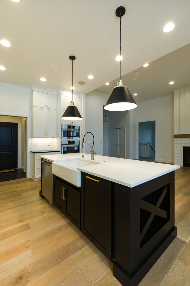 Open concept kitchen - mid-sized transitional l-shaped medium tone wood floor open concept kitchen idea with a farmhouse sink, shaker cabinets, white cabinets, quartzite countertops, white backsplash, subway tile backsplash, stainless steel appliances and an island