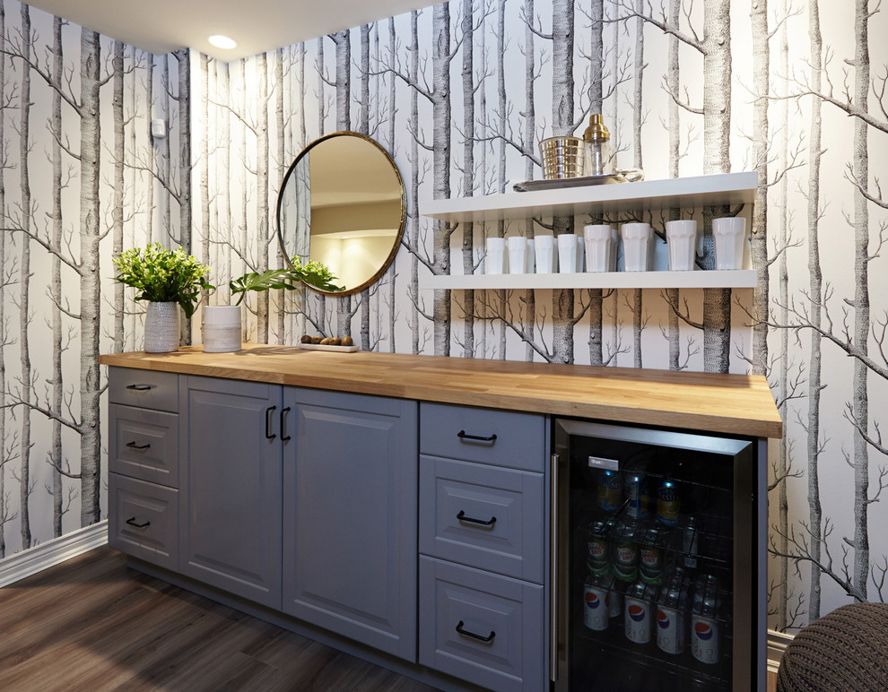 This is an example of a mid-sized eclectic single-wall home bar in Toronto with raised-panel cabinets, wood benchtops, medium hardwood floors, brown floor and blue cabinets.
