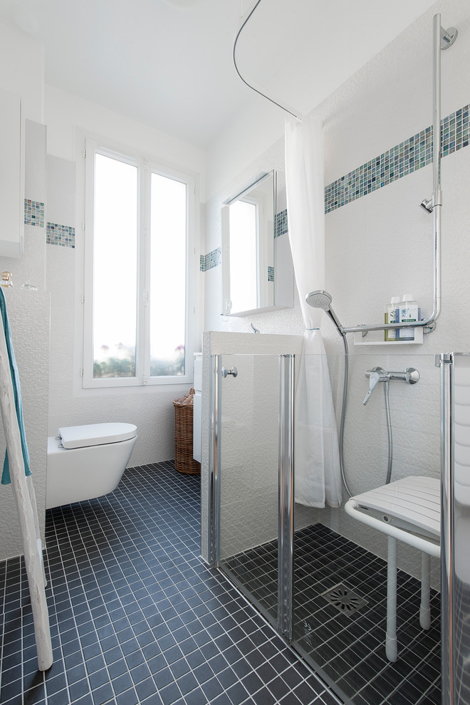 Inspiration for a mid-sized beach style master bathroom in Paris with a curbless shower, a wall-mount toilet, white tile, white walls, a console sink, black floor, a hinged shower door, white benchtops and white cabinets.