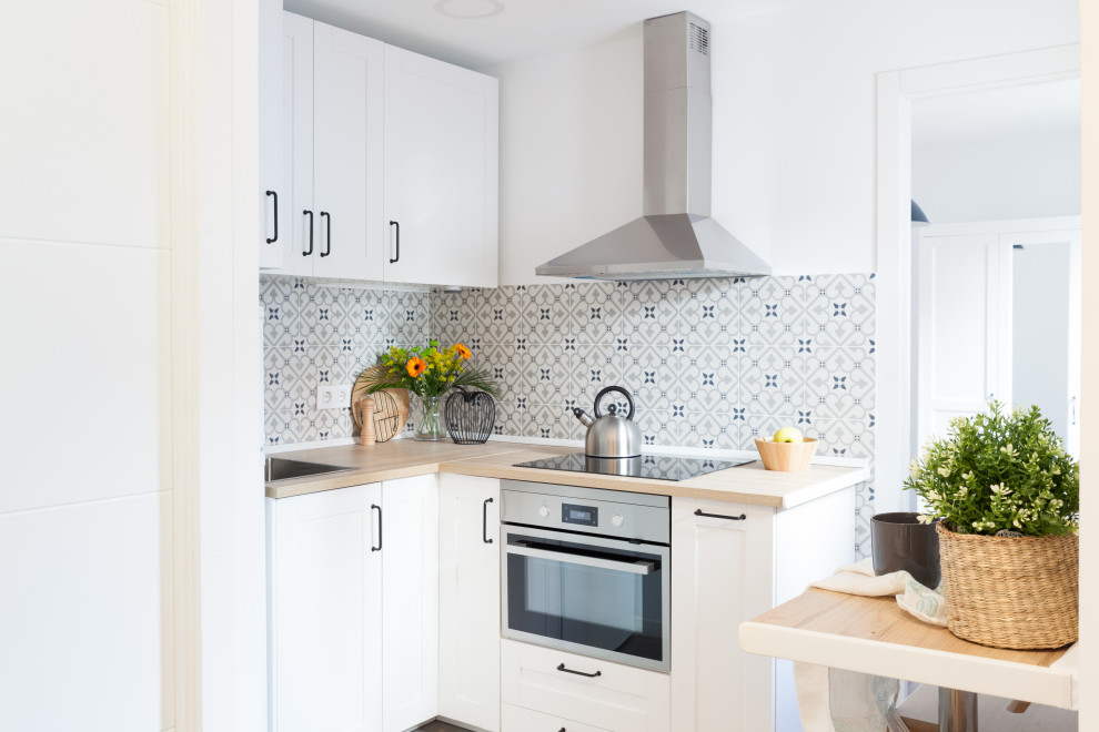 Inspiration for a small scandinavian l-shaped open plan kitchen in Madrid with a drop-in sink, beaded inset cabinets, white cabinets, laminate benchtops, grey splashback, ceramic splashback, white appliances, ceramic floors, no island, grey floor and brown benchtop.