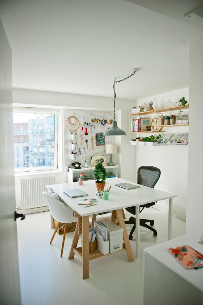 Photo of a scandinavian craft room in London with white walls, painted wood floors and a freestanding desk.