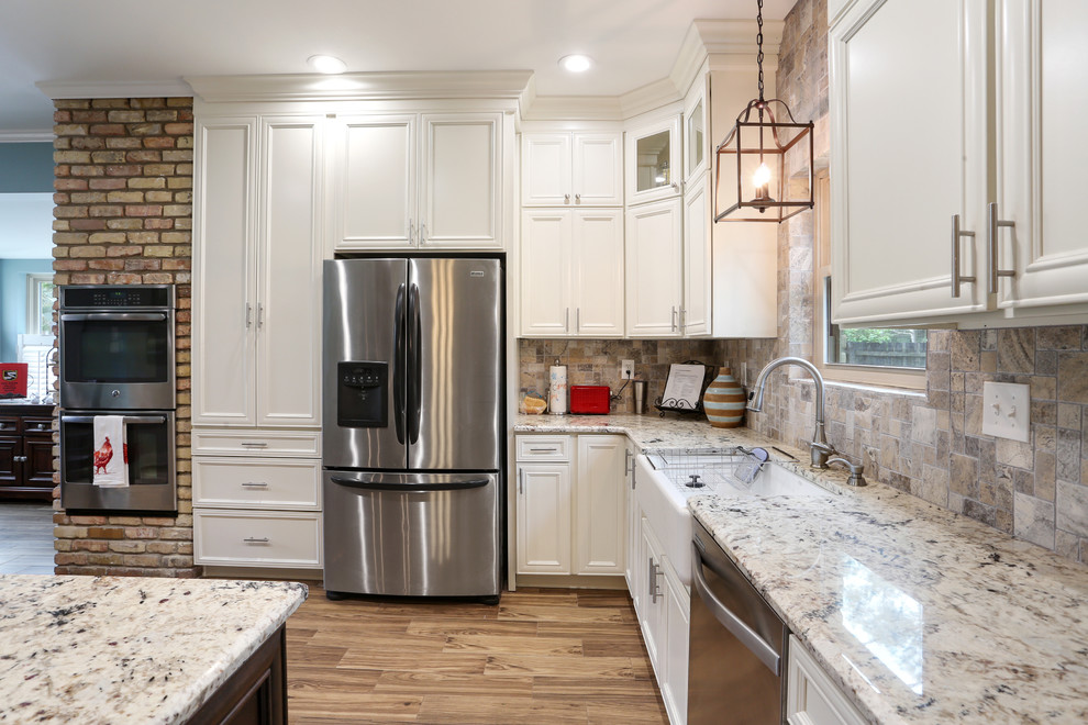 This is an example of a large traditional l-shaped eat-in kitchen in New Orleans with a farmhouse sink, recessed-panel cabinets, white cabinets, granite benchtops, beige splashback, stone tile splashback, stainless steel appliances, porcelain floors, with island, brown floor and grey benchtop.
