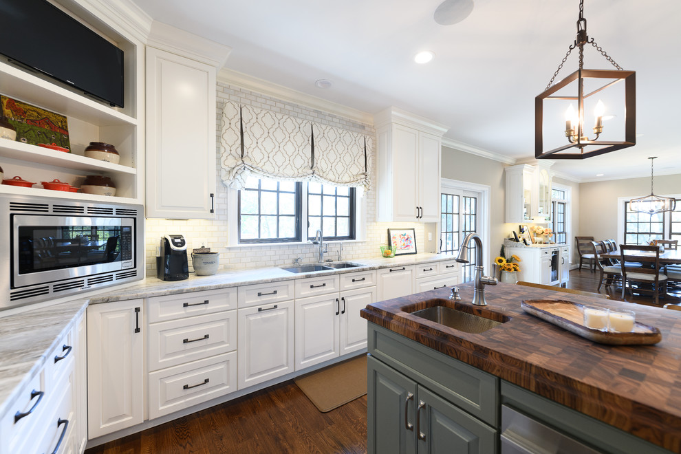 Large transitional l-shaped dark wood floor and brown floor kitchen photo with an undermount sink, raised-panel cabinets, white cabinets, quartzite countertops, white backsplash, marble backsplash, stainless steel appliances and an island