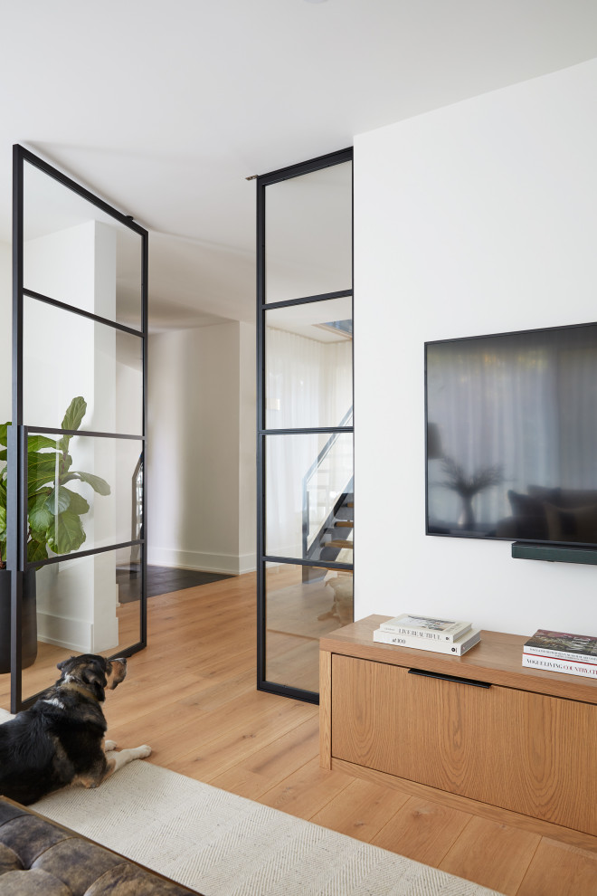 Diseño de sala de estar cerrada contemporánea pequeña con paredes blancas, suelo de madera clara, televisor colgado en la pared y suelo marrón