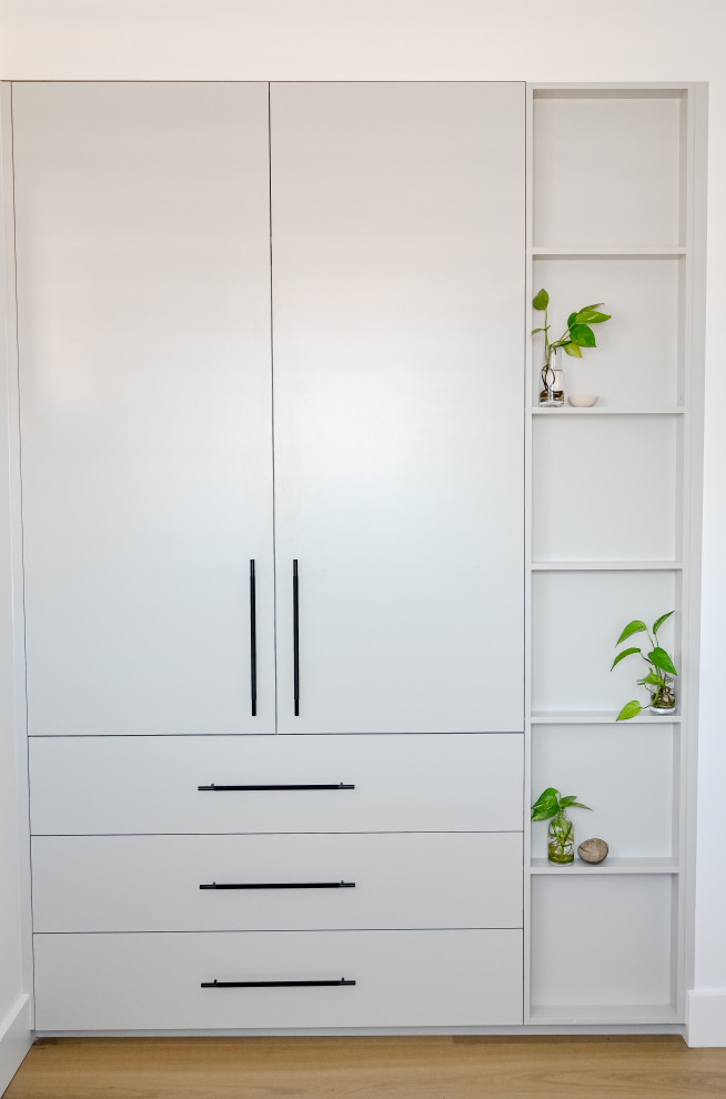 This is an example of a small tropical gender-neutral storage and wardrobe in Sydney with grey cabinets, light hardwood floors and brown floor.