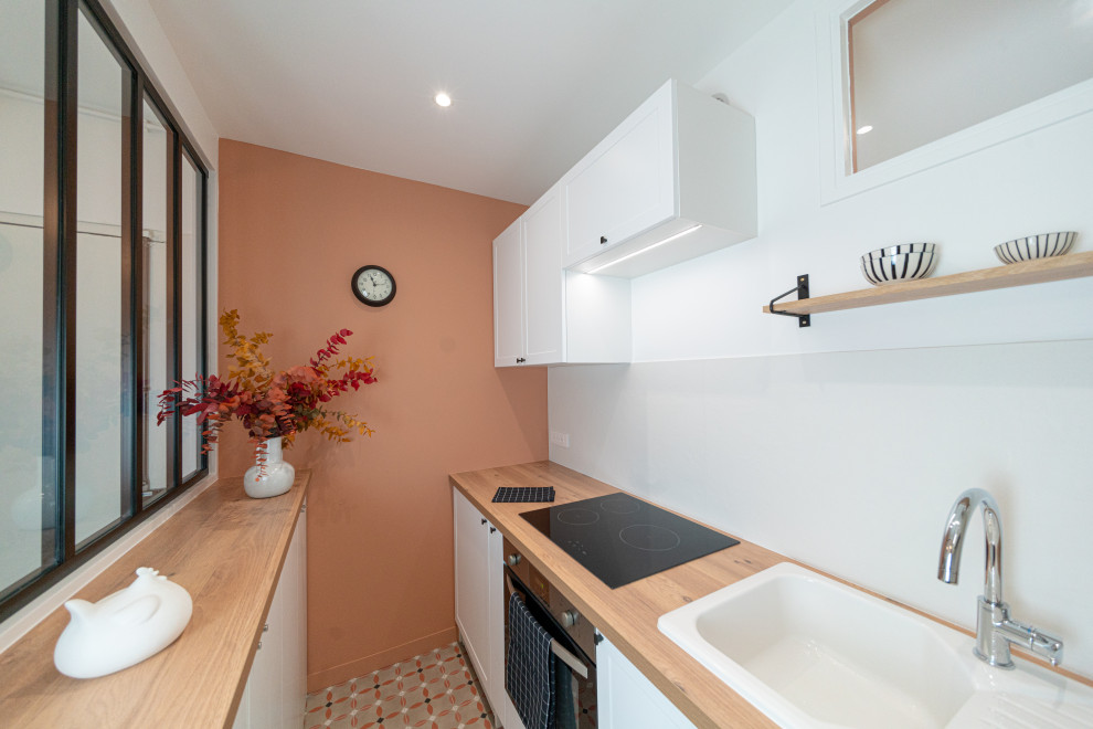 This is an example of a small traditional single-wall separate kitchen in Paris with an undermount sink, flat-panel cabinets, white cabinets, wood benchtops, white splashback, ceramic splashback, cement tiles, panelled appliances, no island, beige floor and brown benchtop.