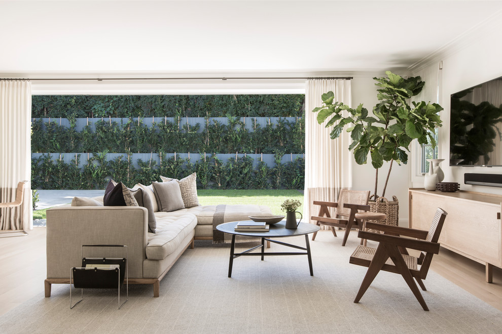 This is an example of a transitional family room in New York with white walls, light hardwood floors, a wall-mounted tv and beige floor.