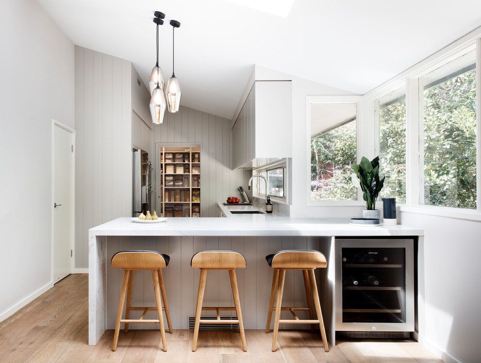 Inspiration for a large contemporary l-shaped eat-in kitchen in Sydney with an undermount sink, flat-panel cabinets, grey cabinets, quartz benchtops, window splashback, stainless steel appliances, medium hardwood floors, a peninsula, brown floor and white benchtop.