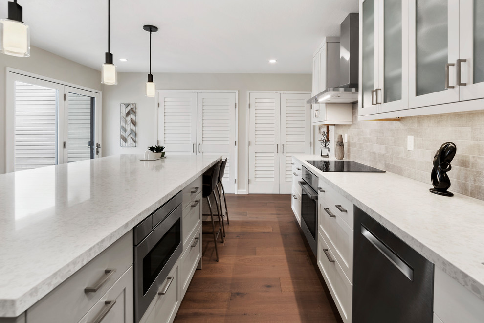 Mid-sized transitional l-shaped medium tone wood floor and brown floor kitchen pantry photo with an undermount sink, shaker cabinets, white cabinets, quartz countertops, beige backsplash, subway tile backsplash, stainless steel appliances, an island and beige countertops