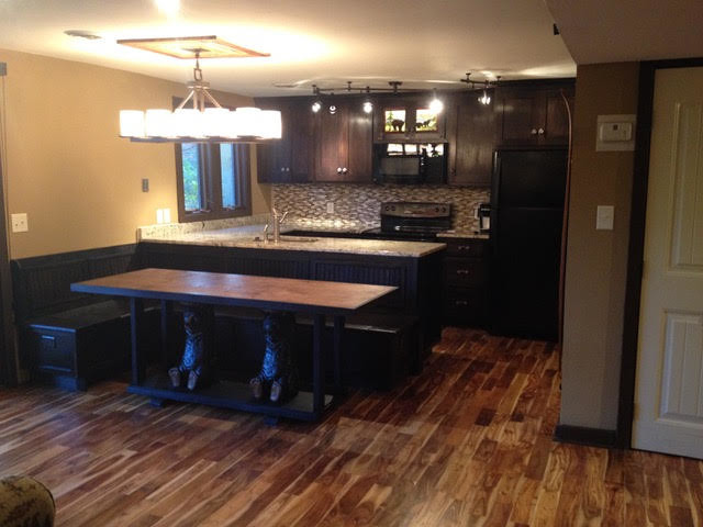 Small mountain style galley medium tone wood floor and brown floor eat-in kitchen photo with an undermount sink, shaker cabinets, dark wood cabinets, granite countertops, brown backsplash, glass tile backsplash, black appliances and a peninsula