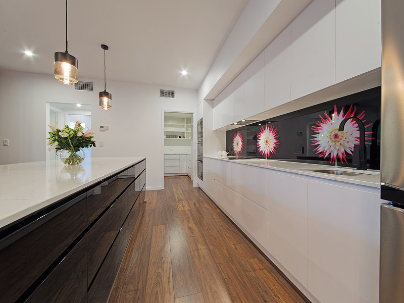 Photo of a large transitional kitchen in Brisbane with an undermount sink, beaded inset cabinets, white cabinets, granite benchtops, black splashback, glass sheet splashback, stainless steel appliances, medium hardwood floors, with island, brown floor and white benchtop.