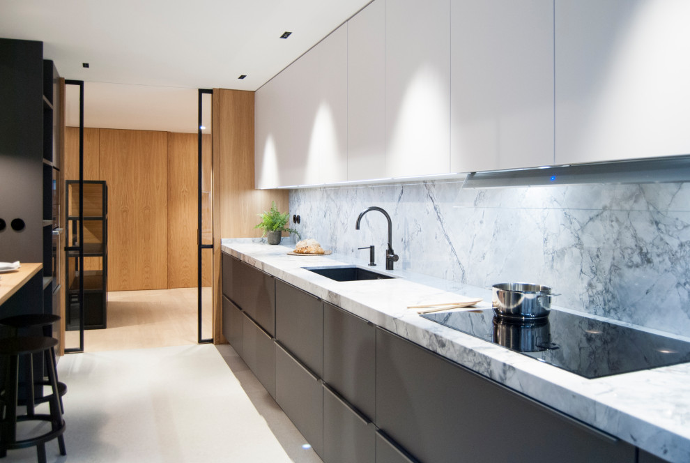 Foto på ett mellanstort funkis vit kök med öppen planlösning, med en undermonterad diskho, släta luckor, grå skåp, marmorbänkskiva, vitt stänkskydd, stänkskydd i marmor, svarta vitvaror och beiget golv