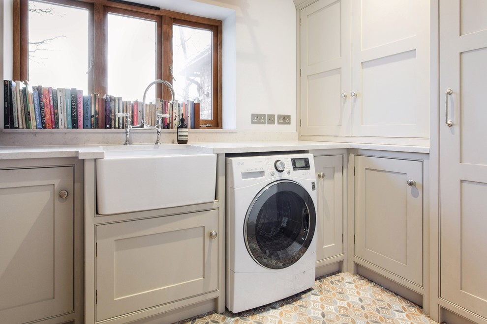 Photo of a small country l-shaped utility room in Sussex with a farmhouse sink, shaker cabinets, beige cabinets, quartzite benchtops, white walls, porcelain floors, a side-by-side washer and dryer, multi-coloured floor and white benchtop.