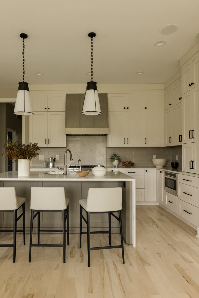 Example of a mid-sized transitional u-shaped light wood floor eat-in kitchen design with an undermount sink, recessed-panel cabinets, beige cabinets, quartz countertops, gray backsplash, ceramic backsplash, stainless steel appliances, an island and white countertops