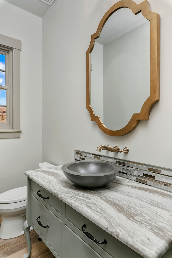 Inspiration for a mid-sized traditional powder room in Boise with flat-panel cabinets, grey cabinets, multi-coloured tile, matchstick tile, grey walls, medium hardwood floors, a vessel sink, granite benchtops, brown floor, grey benchtops and a two-piece toilet.
