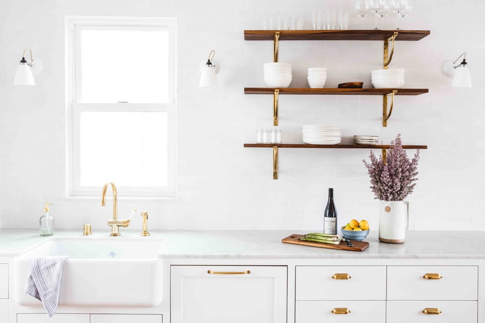 Inspiration for a mid-sized transitional single-wall eat-in kitchen in San Francisco with a farmhouse sink, flat-panel cabinets, white cabinets, marble benchtops, white splashback, ceramic splashback, white appliances, light hardwood floors and with island.