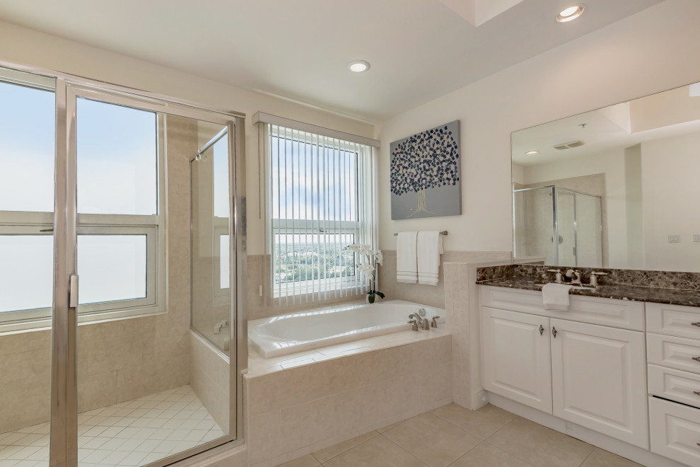 Design ideas for a large modern master bathroom in Tampa with raised-panel cabinets, beige cabinets, a drop-in tub, a corner shower, beige tile, travertine, travertine floors, an undermount sink, granite benchtops, beige floor, a hinged shower door and brown benchtops.