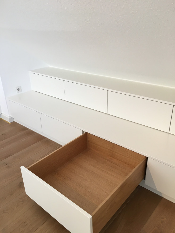 This is an example of a modern storage and wardrobe in Dusseldorf with white cabinets and medium hardwood floors.