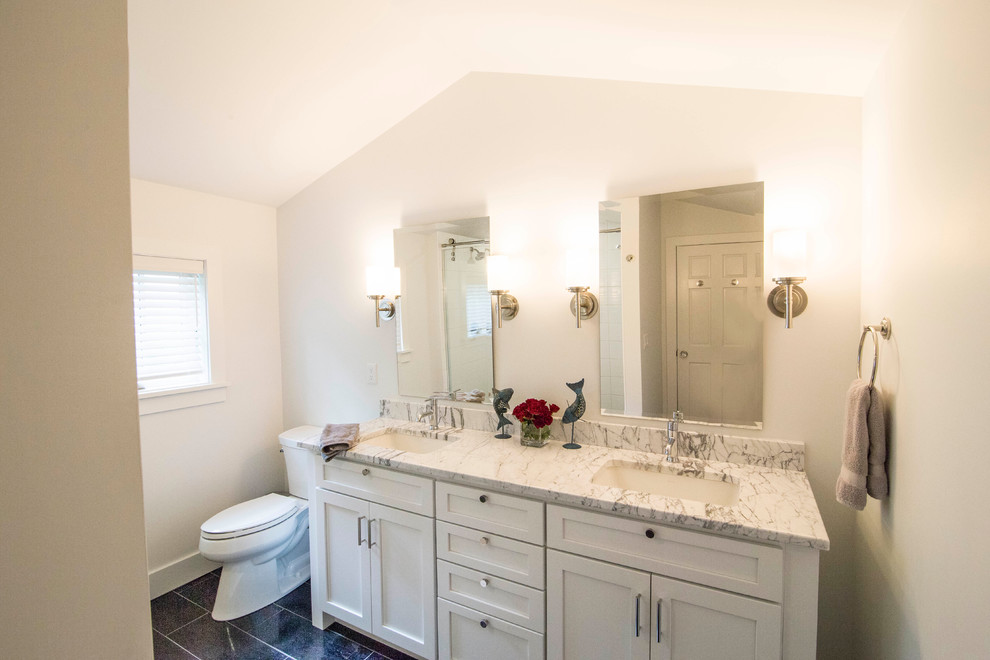 This is an example of a mid-sized contemporary master bathroom in Detroit with shaker cabinets, white cabinets, an alcove shower, a two-piece toilet, white walls, porcelain floors, an undermount sink, marble benchtops, white tile, porcelain tile, black floor, a sliding shower screen and white benchtops.