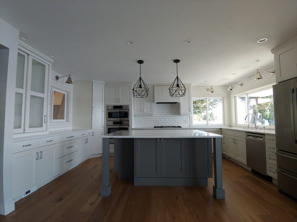 Design ideas for a mid-sized transitional u-shaped eat-in kitchen in Seattle with an undermount sink, shaker cabinets, white cabinets, quartz benchtops, white splashback, ceramic splashback, stainless steel appliances, medium hardwood floors, with island, brown floor and white benchtop.