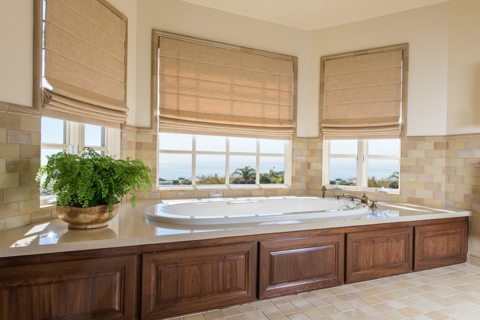 Design ideas for a large traditional master bathroom in Los Angeles with raised-panel cabinets, dark wood cabinets, a drop-in tub, a one-piece toilet, beige tile, gray tile, stone tile, white walls, ceramic floors, an undermount sink and solid surface benchtops.