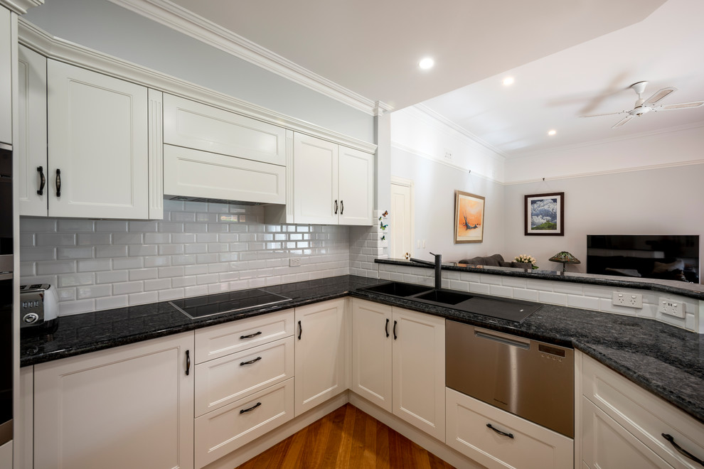 Inspiration for a mid-sized traditional u-shaped separate kitchen in Perth with a drop-in sink, recessed-panel cabinets, white cabinets, granite benchtops, white splashback, porcelain splashback, stainless steel appliances, light hardwood floors, a peninsula, yellow floor and black benchtop.