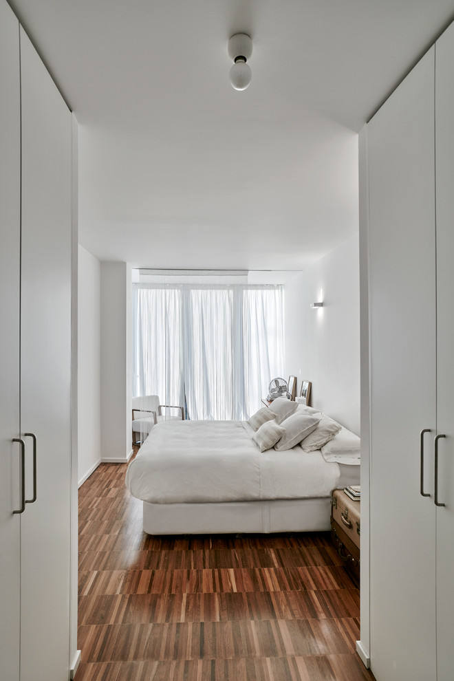 Inspiration for a large contemporary master bedroom in Madrid with white walls, no fireplace, medium hardwood floors and brown floor.