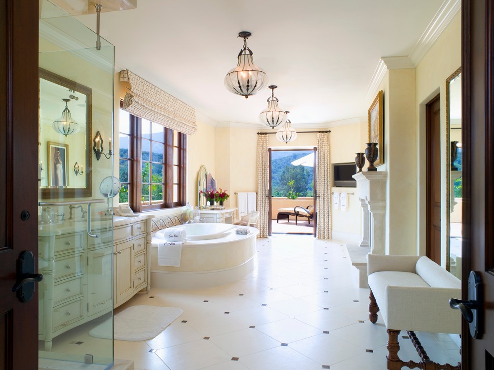 Photo of a mediterranean bathroom in Los Angeles with beige cabinets, a drop-in tub, beige tile and yellow walls.