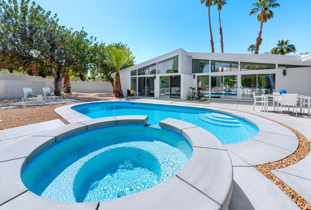 Photo of a large midcentury backyard kidney-shaped natural pool in Other with a hot tub and concrete slab.