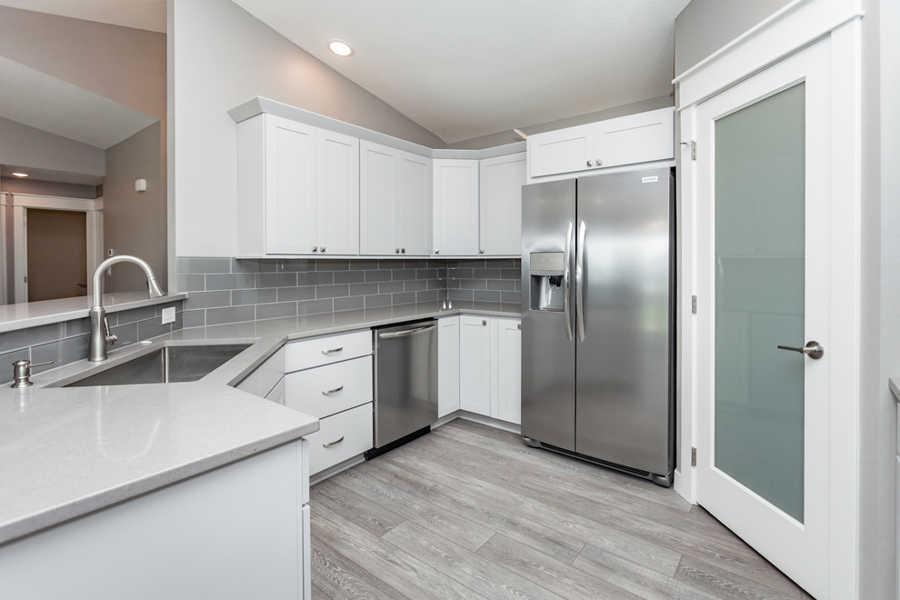 Inspiration for a mid-sized transitional u-shaped medium tone wood floor and gray floor kitchen remodel with an undermount sink, shaker cabinets, white cabinets, quartz countertops, gray backsplash, ceramic backsplash, stainless steel appliances, no island and gray countertops