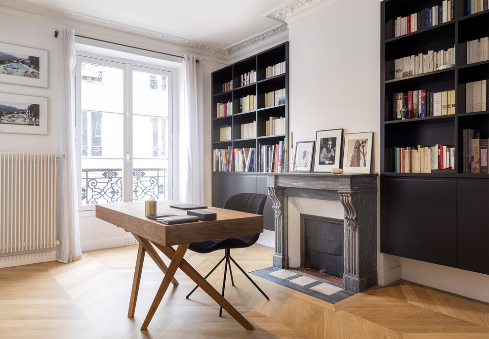 Design ideas for a large transitional home office in Paris with a library, white walls, light hardwood floors, a standard fireplace, a stone fireplace surround, a freestanding desk and beige floor.