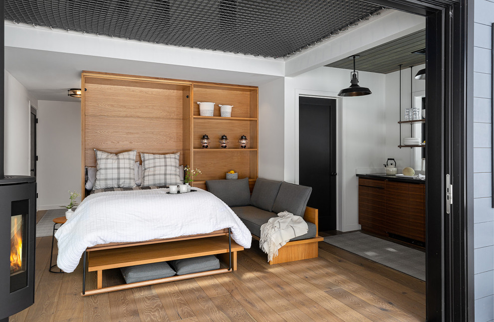 Modelo de dormitorio tipo loft y abovedado contemporáneo pequeño con paredes blancas, suelo de madera en tonos medios y estufa de leña