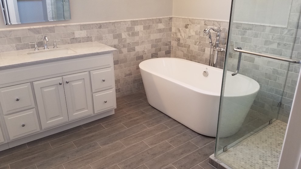 Photo of a mid-sized contemporary master bathroom in Houston with raised-panel cabinets, white cabinets, a freestanding tub, an alcove shower, gray tile, multi-coloured tile, white tile, marble, multi-coloured walls, ceramic floors, an undermount sink, marble benchtops, grey floor and a hinged shower door.