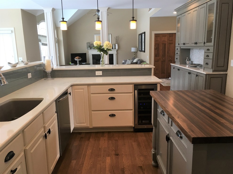 Example of a mid-sized transitional u-shaped light wood floor eat-in kitchen design in New York with an undermount sink, raised-panel cabinets, white cabinets, solid surface countertops, gray backsplash, glass tile backsplash, stainless steel appliances and an island