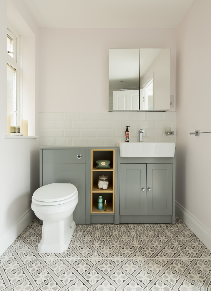 This is an example of a mid-sized transitional powder room in London with recessed-panel cabinets, a one-piece toilet, a drop-in sink, green cabinets, white walls and wood benchtops.