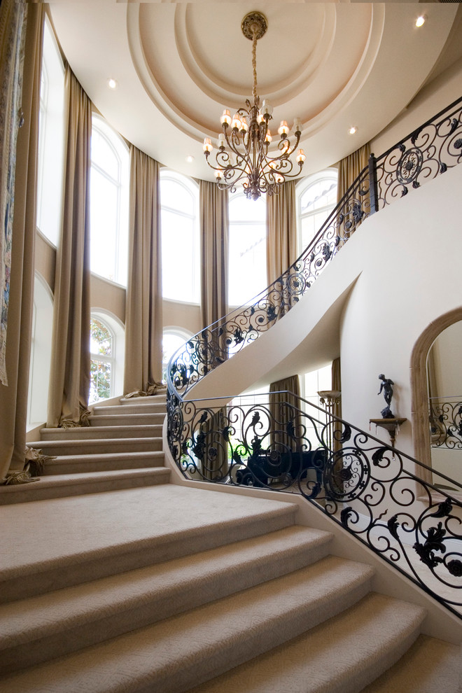 This is an example of an expansive mediterranean carpeted curved staircase in Las Vegas with carpet risers and metal railing.