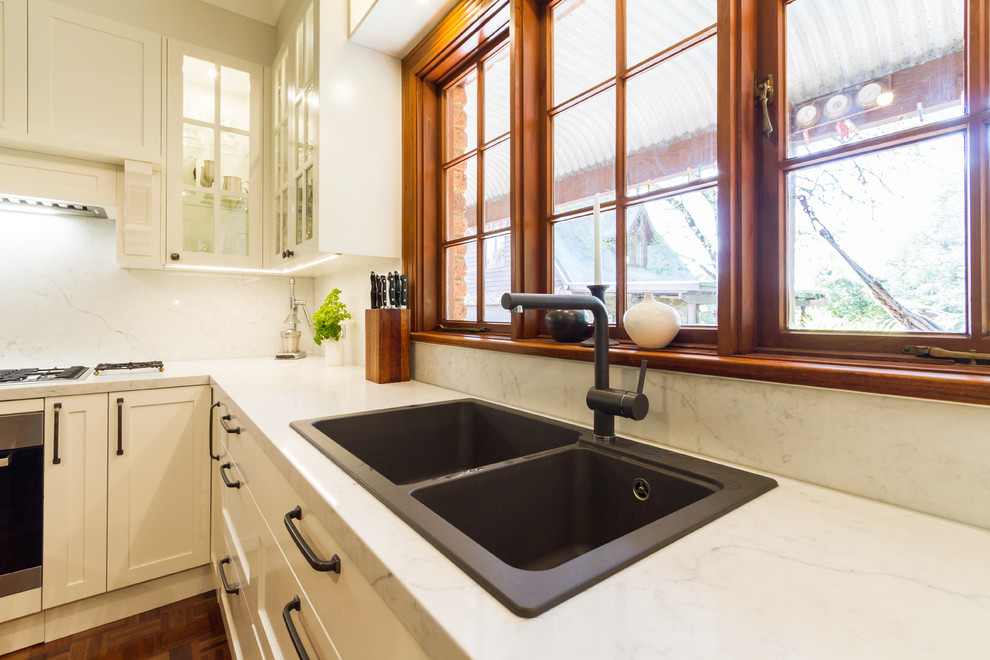 Mid-sized traditional u-shaped eat-in kitchen in Melbourne with a drop-in sink, shaker cabinets, white cabinets, marble benchtops, white splashback, marble splashback, stainless steel appliances, medium hardwood floors, a peninsula, brown floor and white benchtop.
