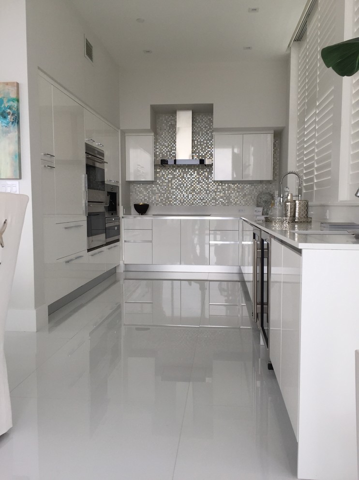 Inspiration for a mid-sized modern u-shaped eat-in kitchen in Miami with an undermount sink, flat-panel cabinets, white cabinets, solid surface benchtops, grey splashback, mosaic tile splashback, panelled appliances, vinyl floors, no island and white floor.