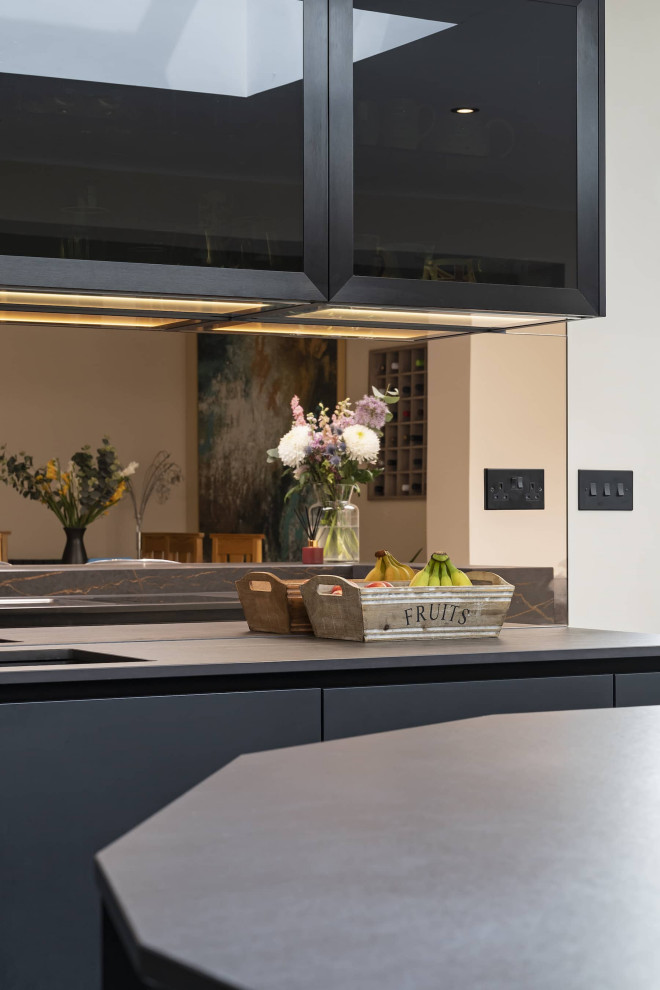 Inspiration for a mid-sized modern eat-in kitchen in Oxfordshire with an integrated sink, glass-front cabinets, black cabinets, quartzite benchtops, glass sheet splashback, black appliances, ceramic floors, with island, grey floor, multi-coloured benchtop and coffered.