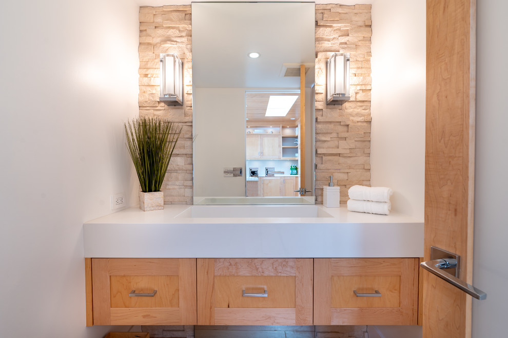 This is an example of an expansive contemporary bathroom in Los Angeles with shaker cabinets, light wood cabinets, a wall-mount toilet, beige tile, stone tile, white walls, porcelain floors, an integrated sink, engineered quartz benchtops, beige floor and white benchtops.