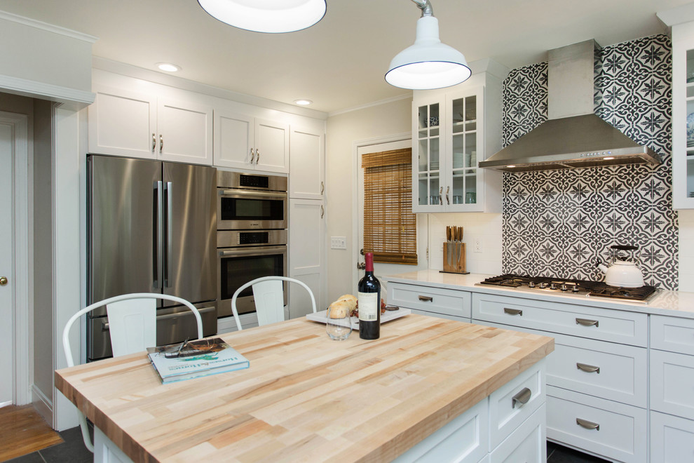 Photo of a mid-sized country u-shaped kitchen in Boston with a farmhouse sink, shaker cabinets, white cabinets, solid surface benchtops, stainless steel appliances, cement tiles, with island, grey floor, white splashback and ceramic splashback.