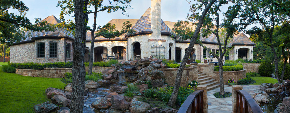Photo of a large country one-storey beige exterior in Dallas with stone veneer and a hip roof.