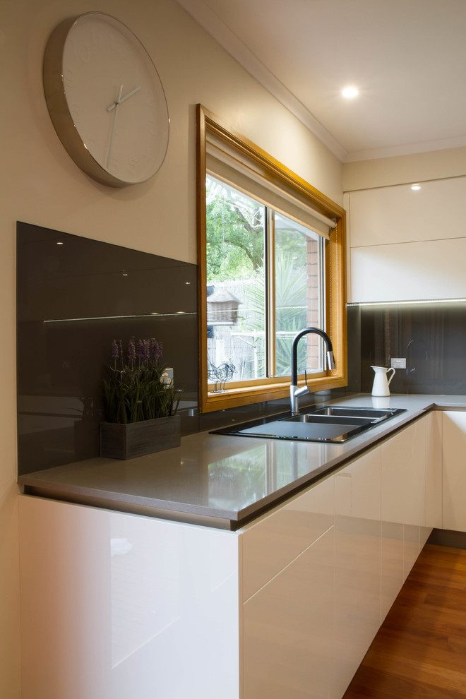Design ideas for a large modern l-shaped eat-in kitchen in Melbourne with flat-panel cabinets, quartz benchtops, metallic splashback, glass sheet splashback, medium hardwood floors and with island.