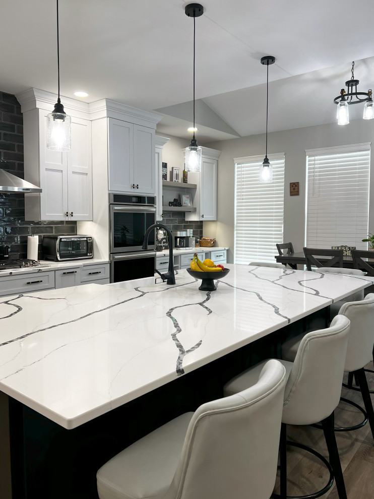 Large transitional single-wall vinyl floor and beige floor eat-in kitchen photo with a farmhouse sink, shaker cabinets, white cabinets, quartz countertops, black backsplash, subway tile backsplash, stainless steel appliances, an island and white countertops